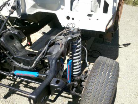 1982 Ford Bronco - The chassis and suspension of a vehicle are shown, with a partial white body shell and a tire.