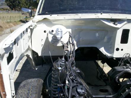 1982 Ford Bronco - The engine bay of a white vehicle is shown, with many components removed and wiring exposed.