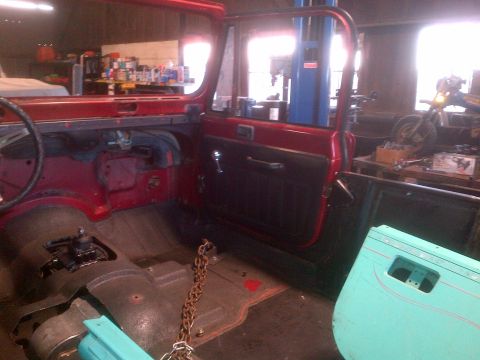 1985 Jeep CJ7 - Interior view of a red Jeep, likely from the 1980s, with its door open and a spare door on the right.