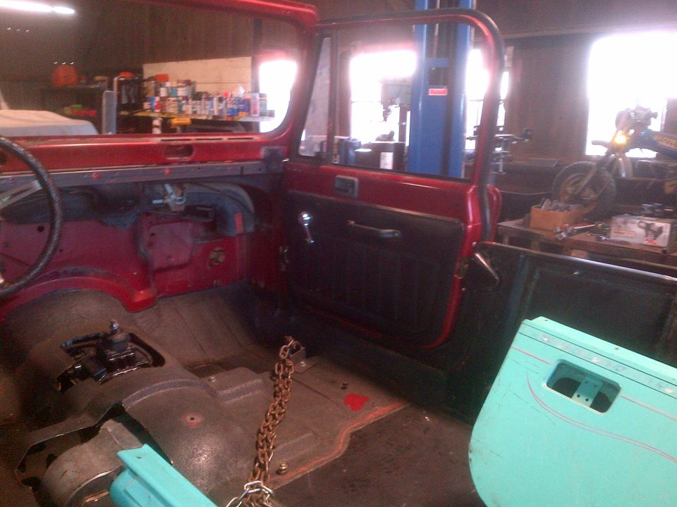 Red Jeep interior with open door, showing floor, steering wheel, and dashboard. A turquoise door lies nearby