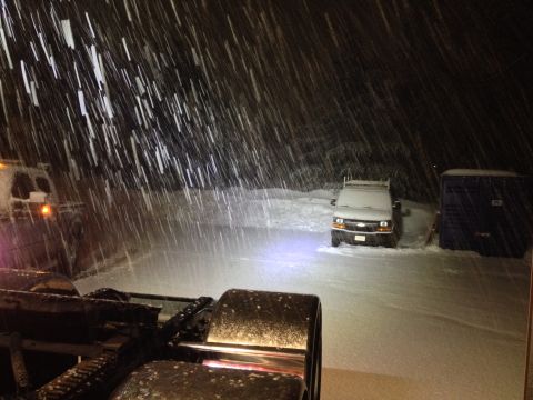 2003 Peterbilt 379 - A truck's front end is visible in the foreground during a heavy snowfall, with a white van parked in the background.