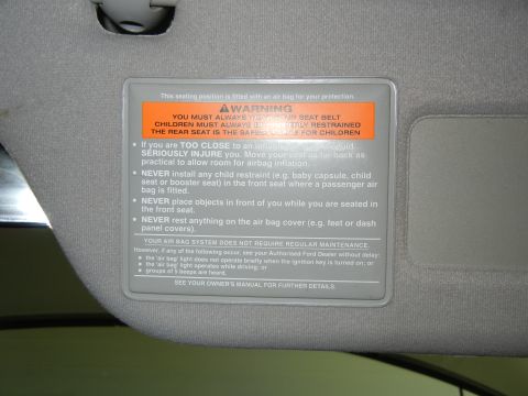 1999 Ford Fairlane - Sun visor warning label details airbag safety and seat belt usage for passengers.