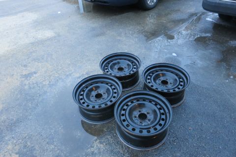 2001 Ford Crown Victoria - Four black steel wheels are shown on wet pavement, likely awaiting installation or removal from a vehicle.