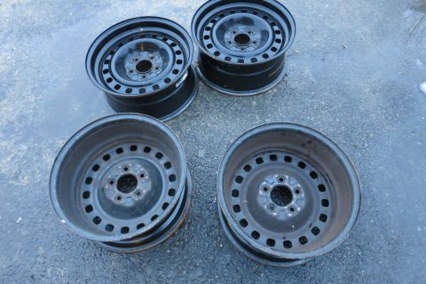 2001 Ford Crown Victoria - A set of four used steel wheels are shown resting on a wet, asphalt surface.