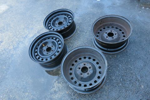 2001 Ford Crown Victoria - A set of four used steel wheels are displayed on a wet, dark surface.