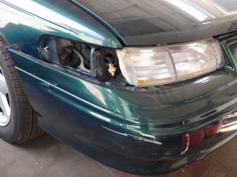 1993 Ford Taurus - Front driver side of a 1993 Ford Taurus, missing headlight assembly. The bumper shows signs of wear.