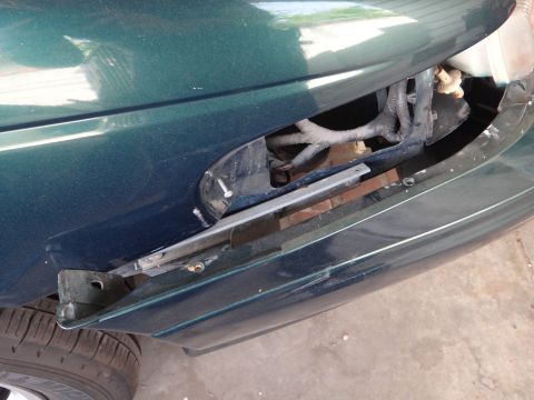 1993 Ford Taurus - Close-up of a damaged green 1993 Ford Taurus front fender, revealing exposed wiring and a broken bumper.