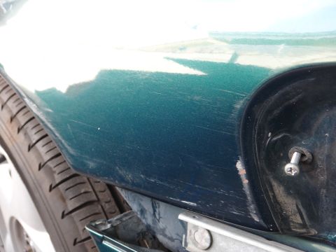 1993 Ford Taurus - Close-up of a damaged green car fender, showing extensive scratches and a screw fastener.