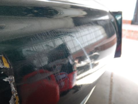1993 Ford Taurus - Close-up of a damaged dark green car panel, showing numerous scratches and peeling tape.