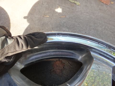 1993 Ford Taurus - Close-up of a damaged chrome wheel rim with visible rust and a gloved hand.