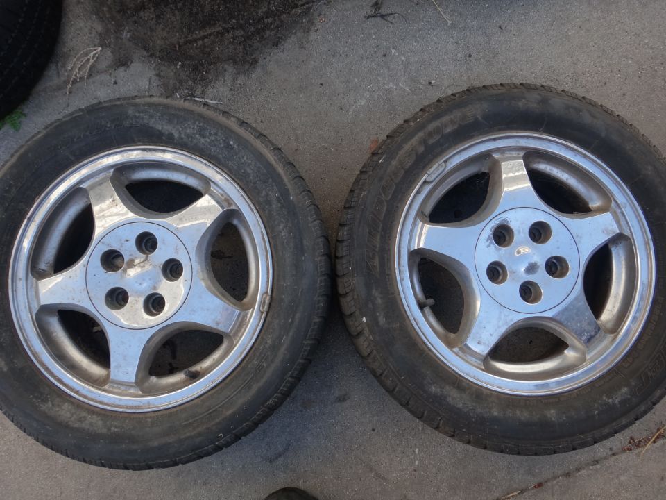 Two alloy wheels with tires on concrete. The wheels have a five-spoke design