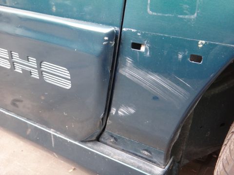 1993 Ford Taurus - The side panel of a green van shows significant damage, including deep scratches and two empty square cutouts.