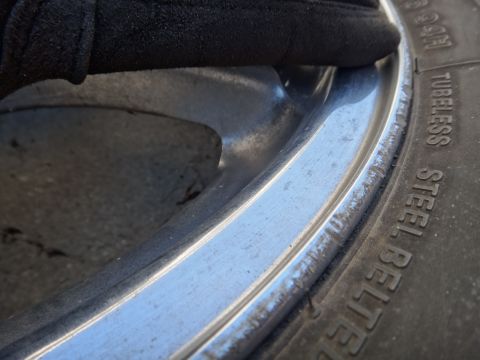 1993 Ford Taurus - A gloved hand rests on the edge of a worn chrome wheel rim next to a tire.