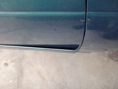 1993 Ford Taurus - Close-up of a green car's lower door panel, showing damage to the trim piece.