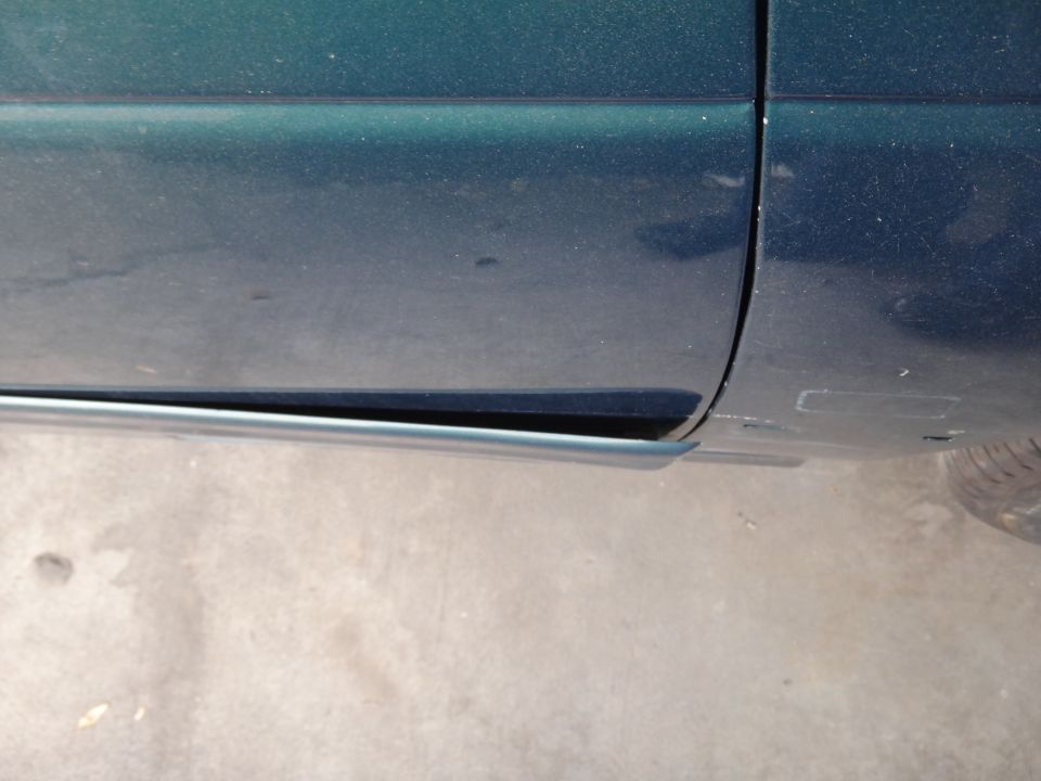 Green car door bottom edge with damage to the lower trim