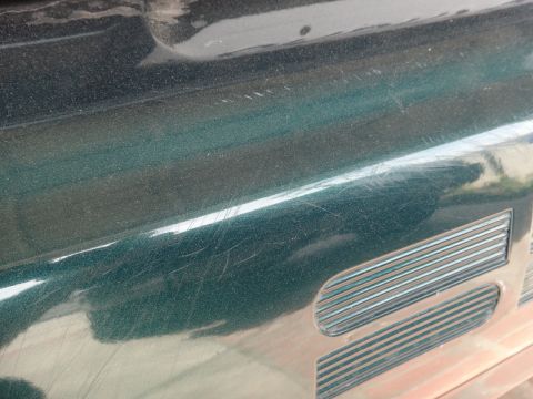 1993 Ford Taurus - Close-up of a dark green fender showing numerous scratches and a section of the vehicle's grille.