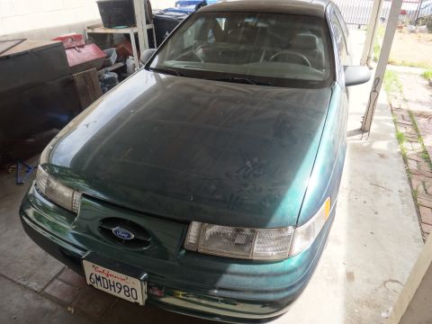 1993 Ford Taurus - A dusty green 1992 Ford Taurus is parked in a garage, showing its front grille and headlights.