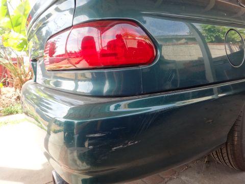 1993 Ford Taurus - The rear bumper and taillight assembly of a dark green vehicle show significant scuffing and scratches.