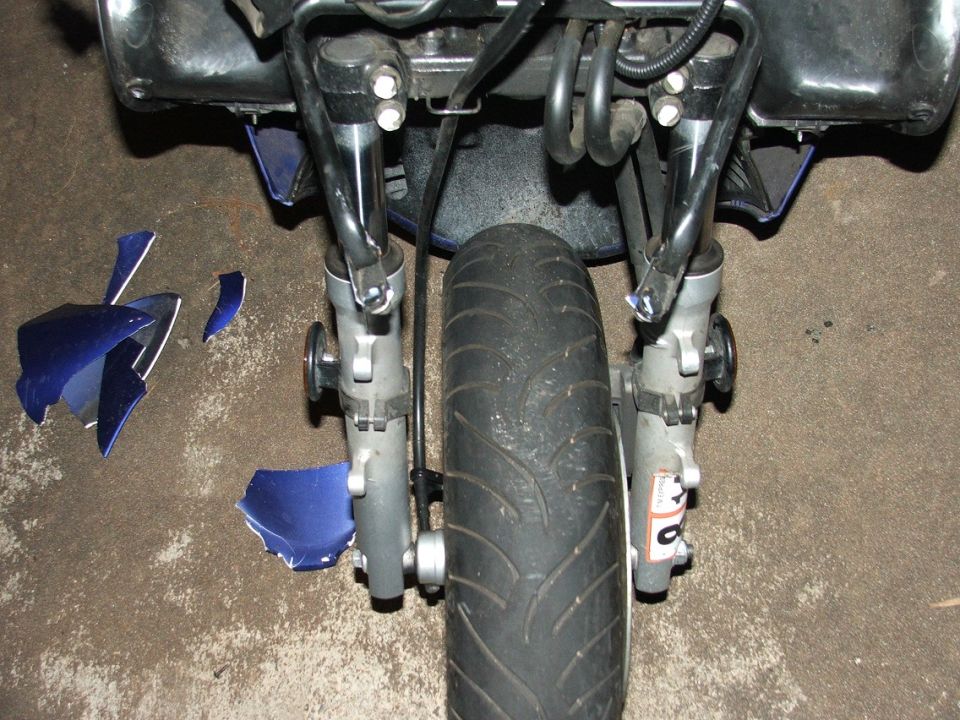 Front wheel and suspension of a motorcycle with broken blue body panels scattered nearby