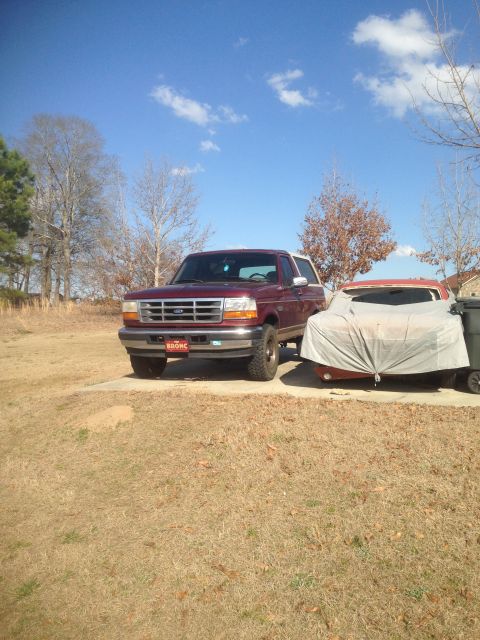 1996 Ford Bronco - A maroon 1996 Ford Bronco is parked on a concrete pad, with another vehicle covered by a tarp to its right.