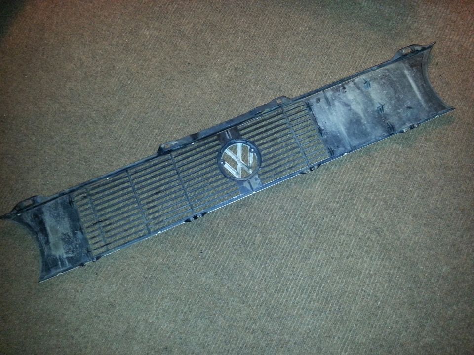 Dark grille with a circular Volkswagen emblem, lying flat on a carpeted surface