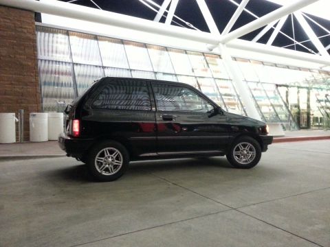 1991 Ford Festiva - A black 1991 Ford Festiva is seen from the side parked in front of a modern building.