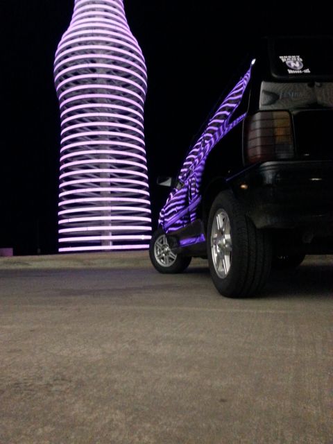1991 Ford Festiva - A customized hatchback is parked at night next to a large, illuminated bottle structure.