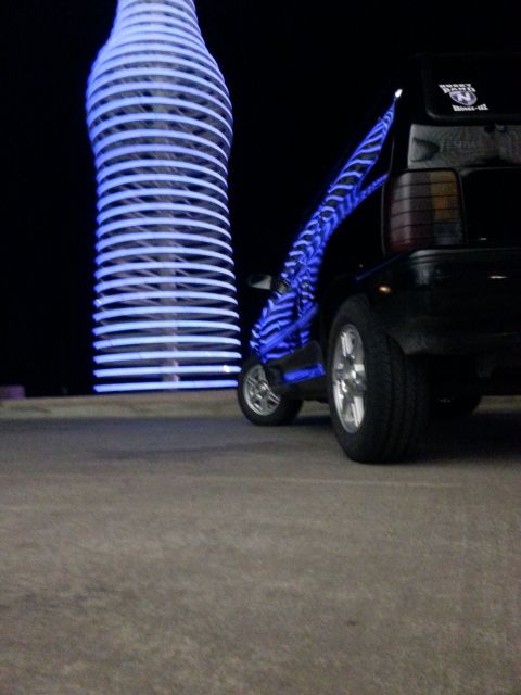 1991 Ford Festiva - A modified scooter with blue lights is parked near a large bottle-shaped sculpture.