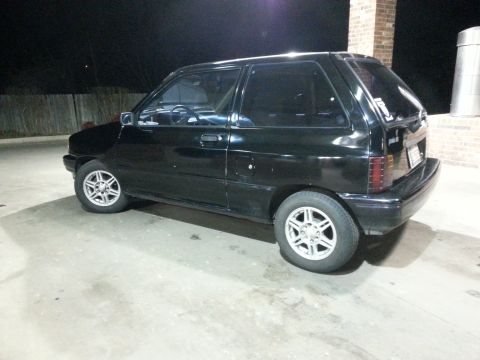 1991 Ford Festiva - This black 1991 Ford Festiva is seen from the 3/4 front angle, parked outdoors at night.