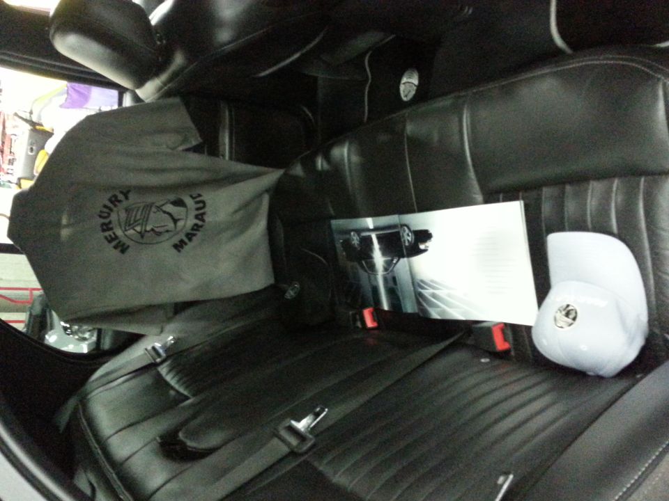 Car interior showing black leather seats, a gray cover with 'MERCURY MARAUDER' logo, a brochure with a car image, and a white cap