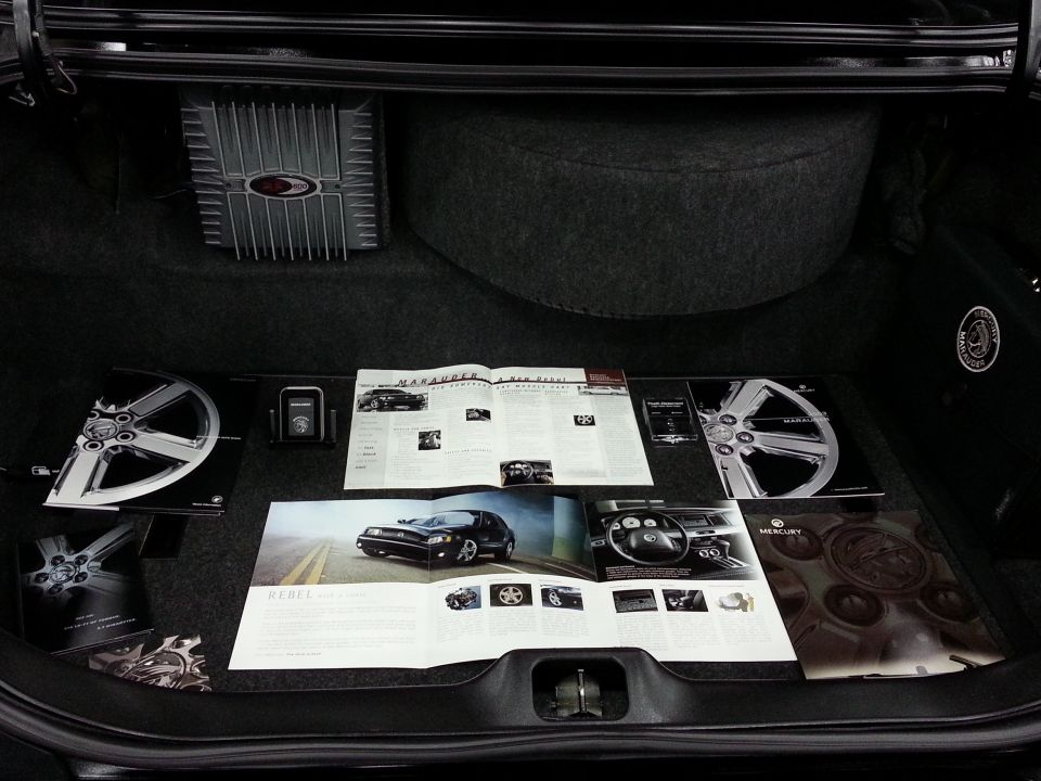 Car trunk with brochures showing a Mercury Marauder, wheels, and interior, plus an amplifier