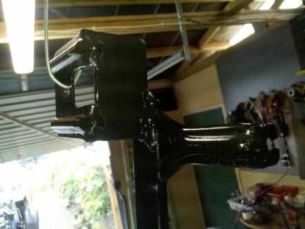 1982 Ford Bronco - A black painted metal component is suspended in a workshop, awaiting further assembly or installation.