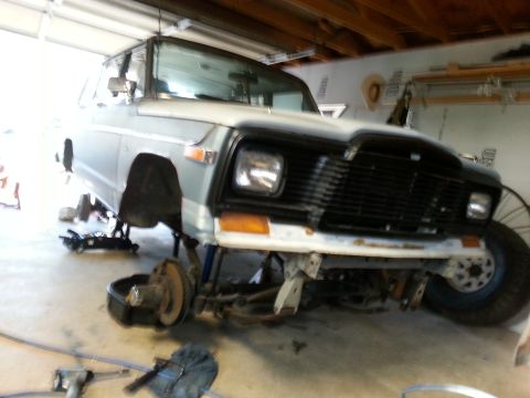 1982 Jeep Wagoneer - Front end of a 1982 Jeep Wagoneer undergoing maintenance, with wheels removed and vehicle supported by jack stands.