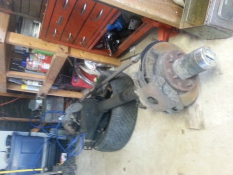1982 Jeep Wagoneer - Close-up of a vehicle's front axle assembly, including the brake system and tire, in a garage setting.