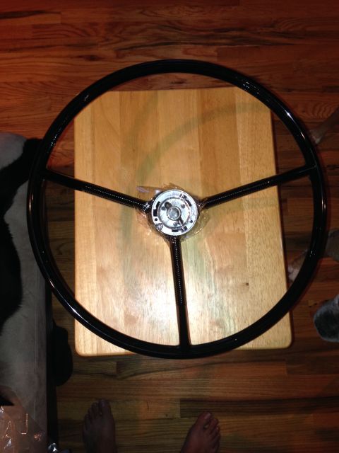 1964 Ford Fairlane - A black steering wheel is shown from above, placed on a wooden surface.