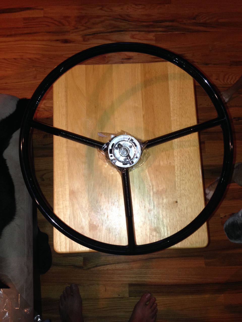 Black three-spoke steering wheel with chrome center hub, resting on a wooden table
