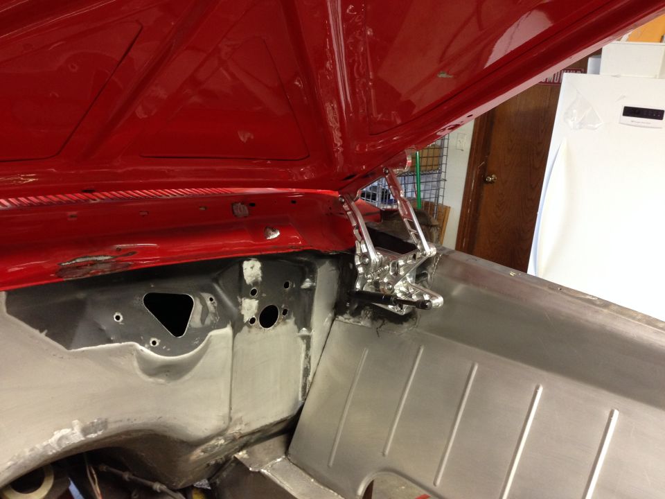 Open red hood showing shiny custom hood hinges and raw metal engine bay structure