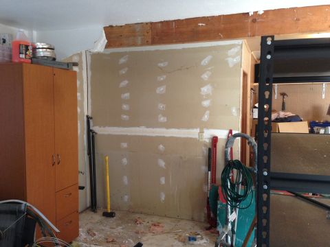 1964 Ford Fairlane - A cluttered garage scene shows a tall wooden cabinet, various tools including a sledgehammer and jacks, and a wall with visible drywall rep…