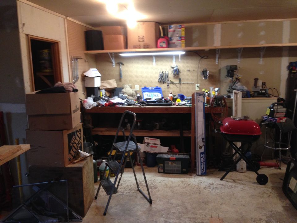 Garage interior with a workbench cluttered with tools and boxes, a red grill, and a step ladder