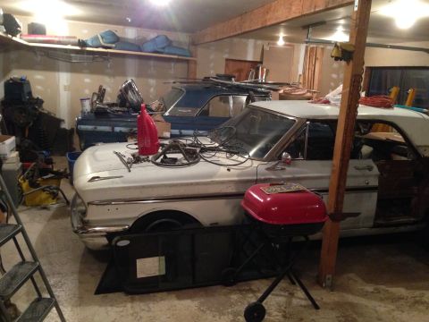 1964 Ford Fairlane - Two cars, a 1964 Ford Fairlane and a blue sedan, sit in a garage with parts and tools around them.