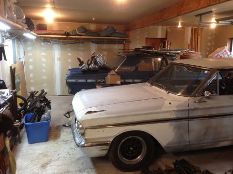 1964 Ford Fairlane - Two vintage cars are parked inside a cluttered garage, one in primer and the other dark blue.