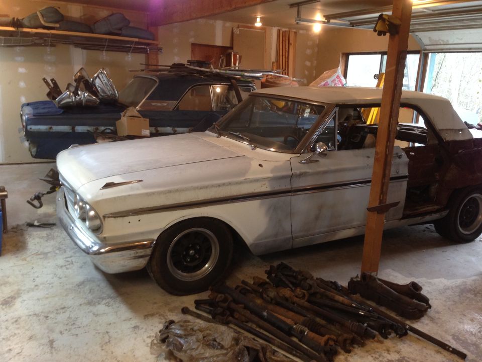 White 1964 Ford Fairlane convertible with a maroon rear quarter panel, in a garage with parts