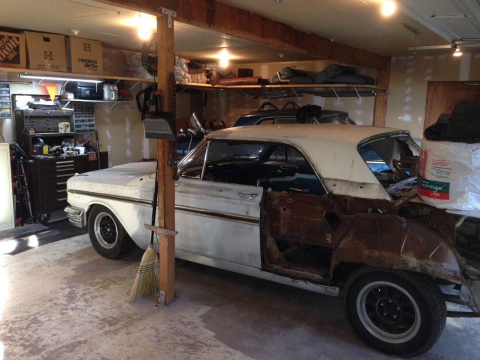 1964 Ford Fairlane project car with doors removed, sitting in a garage next to another car