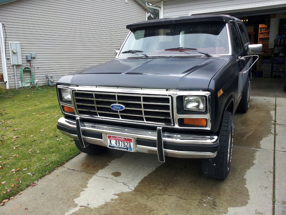 Flat black Ford Bronco front view with chrome grille and bumper, Idaho plate, parked on driveway by garage