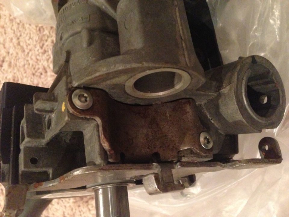 Close-up of removed steering column housing with ignition lock bore and rusty bracket, Torx screws visible
