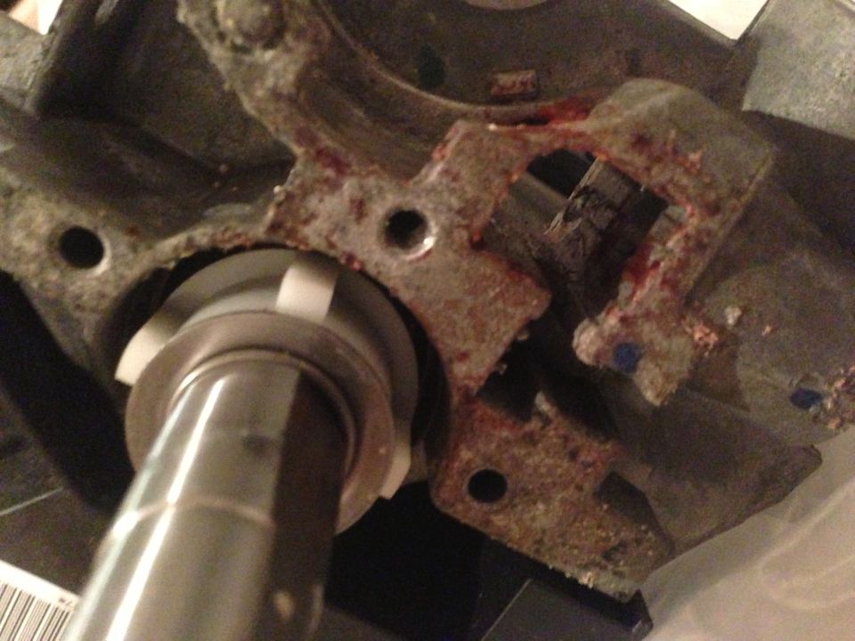 Close-up of corroded cast metal steering column housing with shaft, showing rust-colored residue