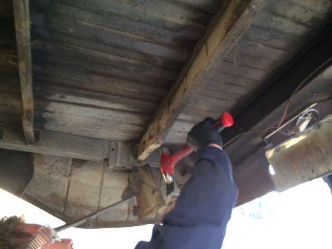 1964 Ford Ranchero - A person works on the underside of a wooden truck bed, hammering a rusted metal support beam.