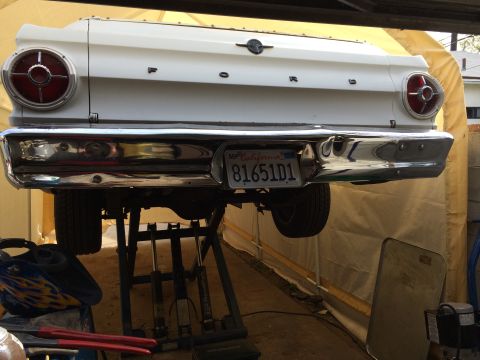 1964 Ford Ranchero - The rear of a white 1964 Ford Ranchero is shown, lifted for maintenance, with its distinctive taillights and chrome bumper visible.
