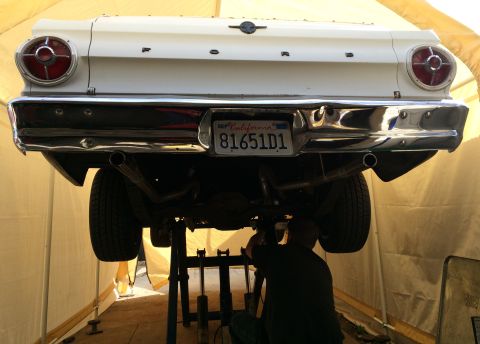 1964 Ford Ranchero - A mechanic works on the exhaust system of a white Ford pickup truck that is raised on a lift.