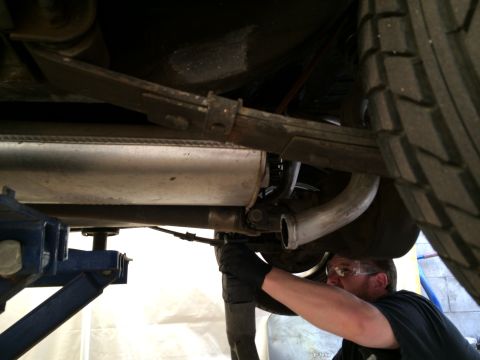 1964 Ford Ranchero - A mechanic works on the exhaust system of a vehicle, with a leaf spring and tire visible.